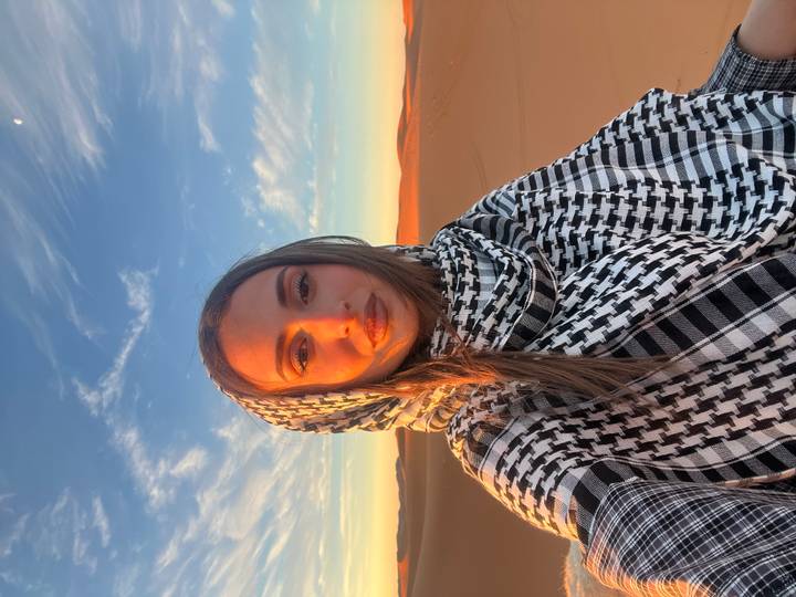 Portrait of a traveller wrapped in keffiyeh with endless sand dunes and blue sky behind her.