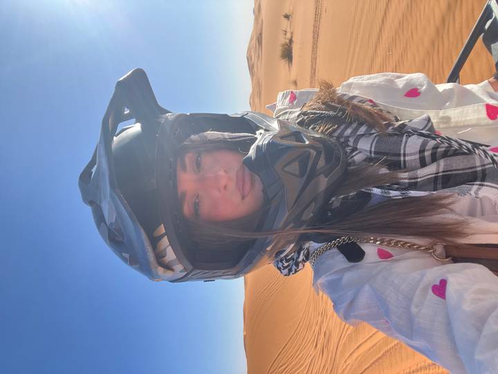Portrait of a woman in off-road helmet standing amid saffron desert sands and blue sky.