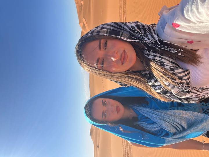 Bright portrait of two female friends in desert attire with vast dunes in background.