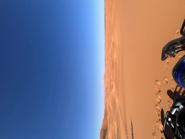 Wide blue sky over endless desert plain with quad-bike handlebars visible at bottom edge.