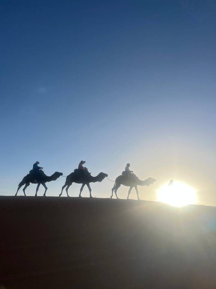 Silhouettes of three riders on camels against a glowing desert sunrise