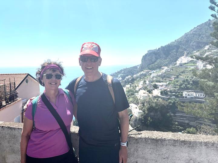 Smiling couple with backpacks pose on a terrace overlooking terraced hills and the Amalfi coastline