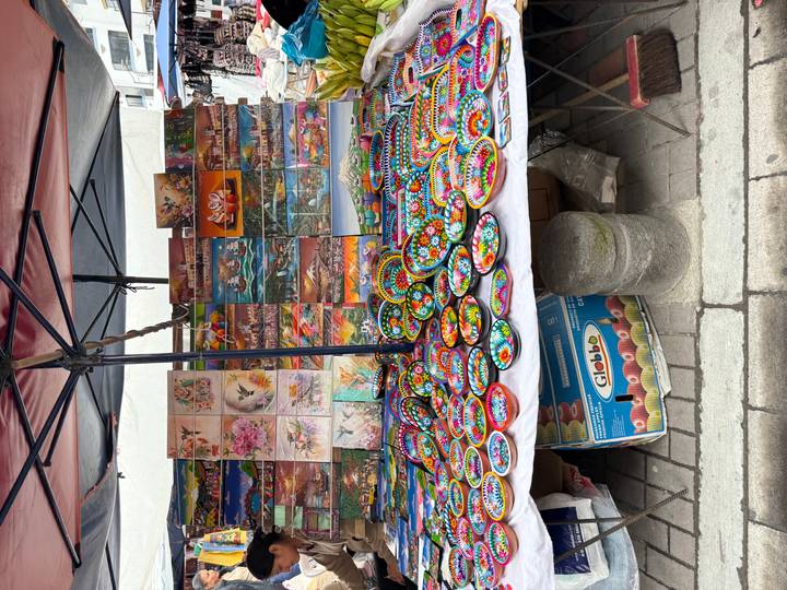 Street market stall displaying brightly painted wooden plates and colorful landscape art.