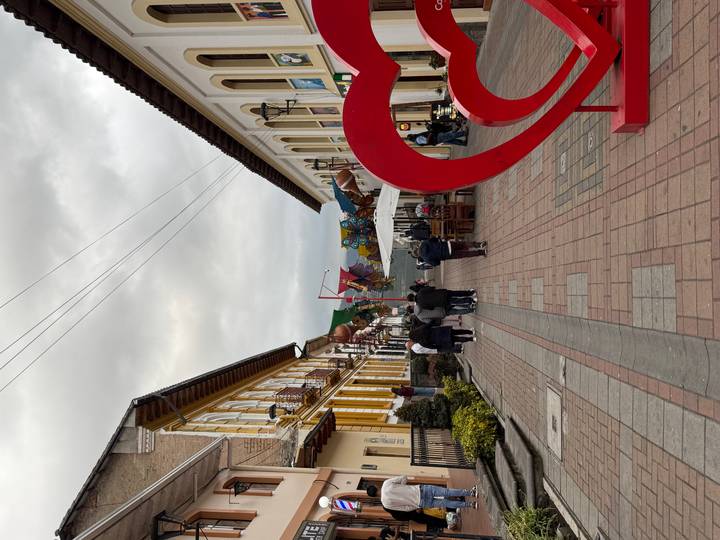 Cobbled colonial street with yellow and white buildings and a large red heart sculpture at dusk.