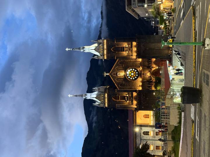Illuminated twin-tower church glows warmly against twilight mountains and a dusky blue sky.