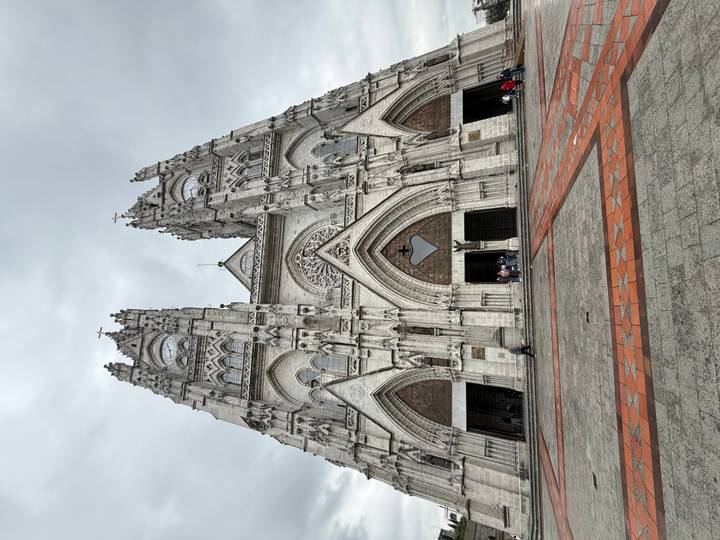 Full façade view of a soaring grey stone basilica with visitors entering beneath pointed arches.