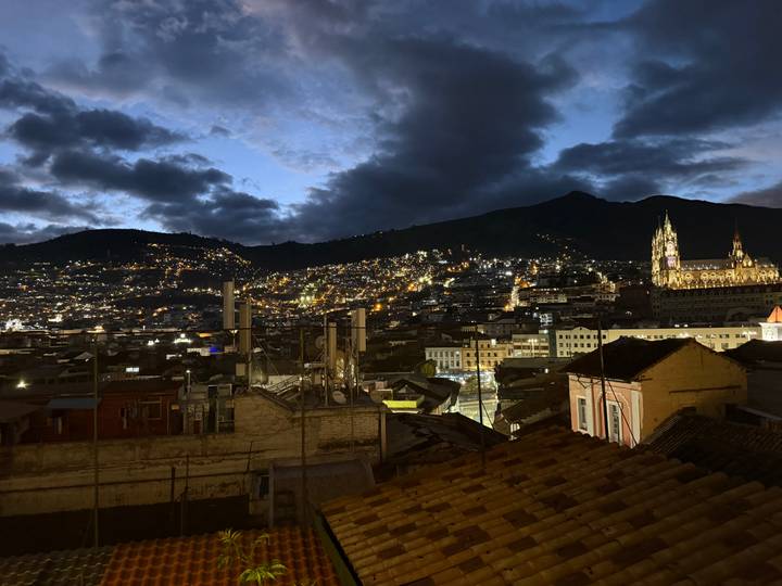 Night panorama of Quito’s twinkling lights with illuminated basilica and mountain silhouette.