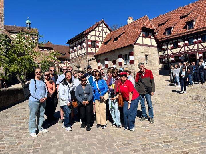 Large tour group smiling in a cobblestoned courtyard surrounded by half-timbered medieval buildings.