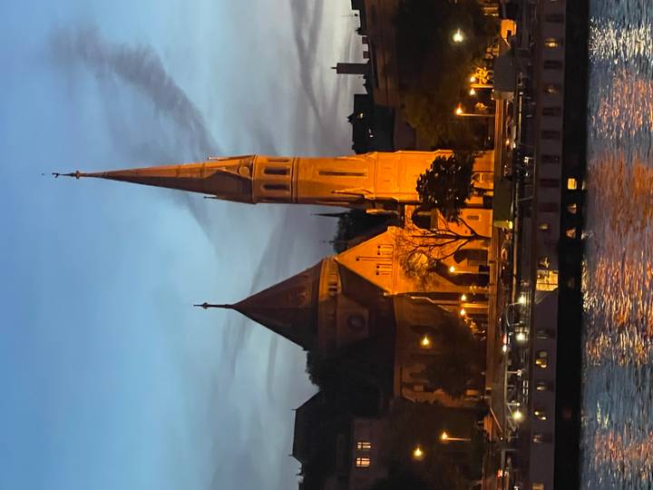 Evening riverside view of an illuminated church with tall steeple along the Danube in Budapest.