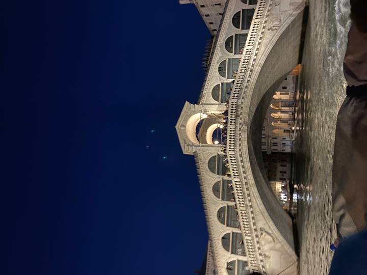 Nighttime photo of the illuminated Rialto Bridge arching over Venice’s Grand Canal.