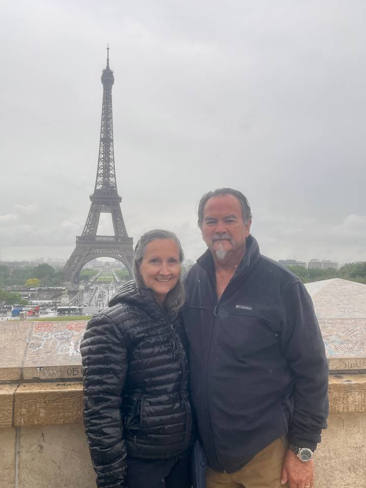 Smiling couple posing on a misty day with the Eiffel Tower rising behind them.