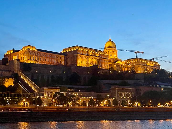Night view of Buda Castle complex illuminated in golden light above the Danube River.