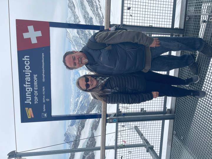 Couple posing at snow-covered Jungfraujoch viewpoint sign labeled 'Top of Europe'.
