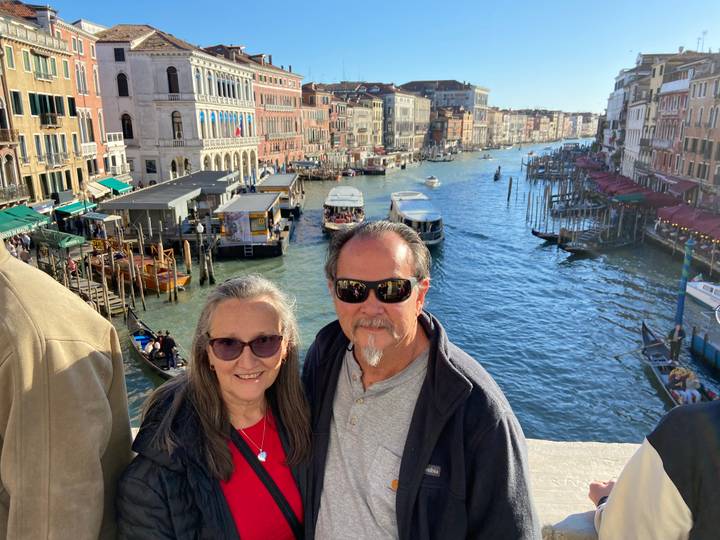Couple leaning on a stone bridge railing with Venice’s Grand Canal bustling with boats behind.