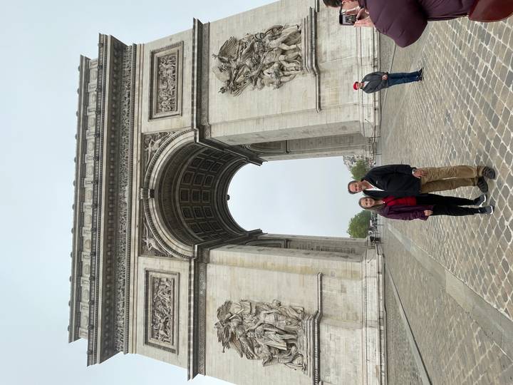 Couple standing beneath the towering Arc de Triomphe on a grey day.