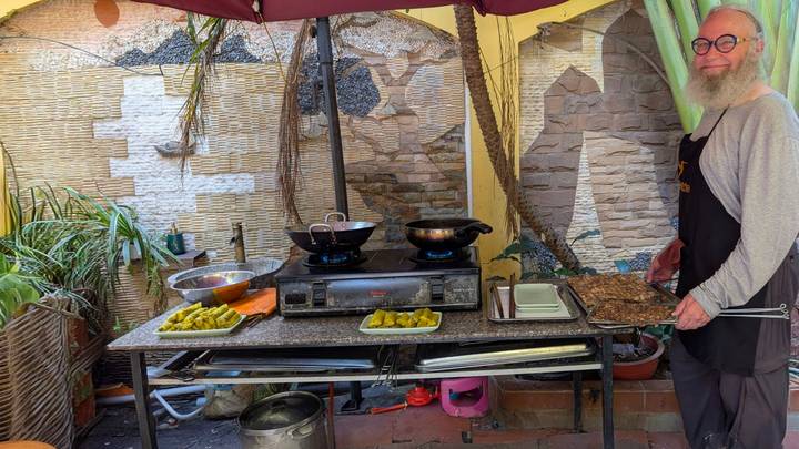 Man preparing traditional Vietnamese dishes on outdoor cooking stoves in a cozy courtyard kitchen.