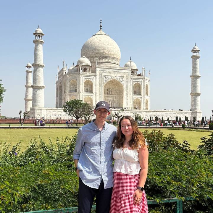Couple posing for a photograph with the Taj Mahal rising majestically behind them.