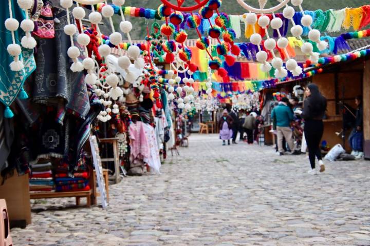 Colorful Andean craft market street with hanging pom-pom decorations and shoppers on a cobblestone lane