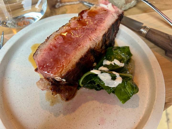 Close-up of a thick medium-rare steak with wilted greens on a restaurant plate