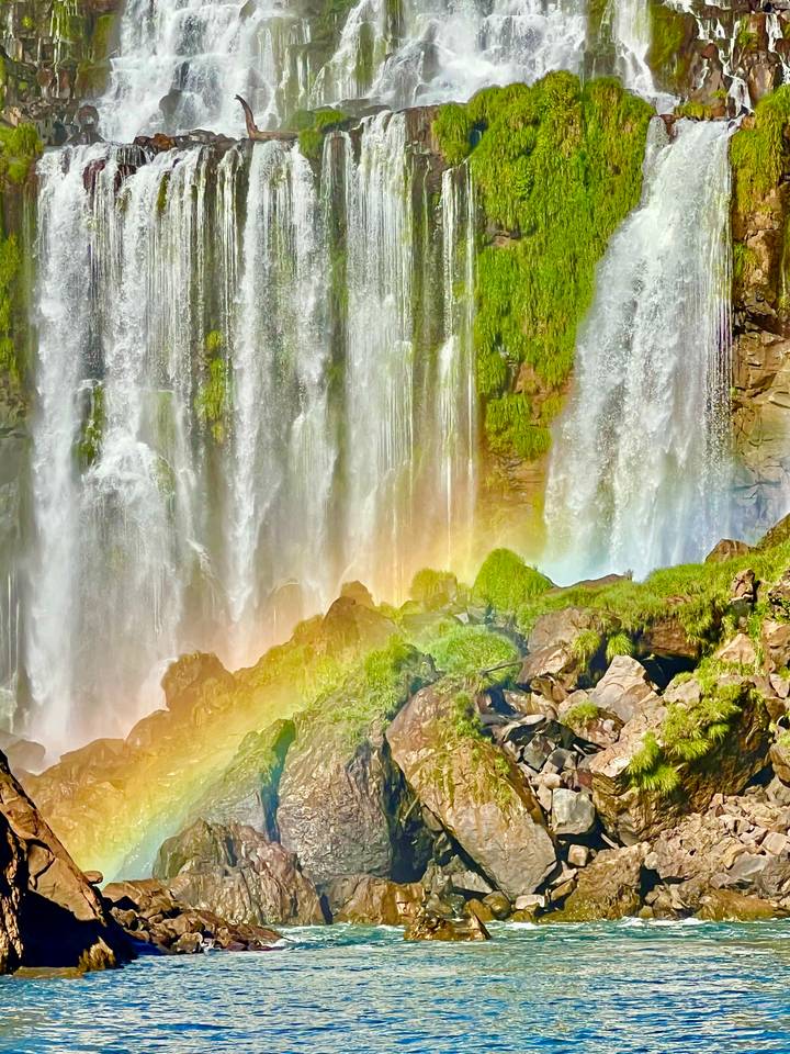 Powerful waterfall curtains with mist and a vivid rainbow over mossy rocks