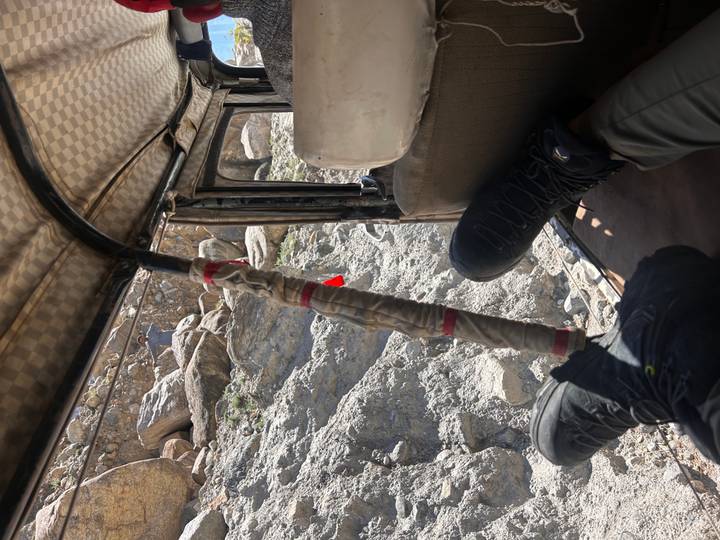 Looking out of a rugged jeep interior, a traveller’s boots rest on the seat as the vehicle navigates a rocky track.