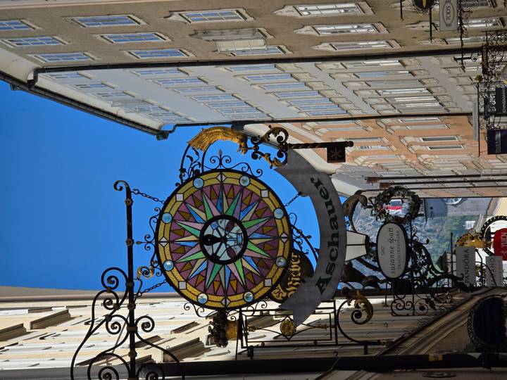 Decorative wrought-iron shop sign with colourful compass motif hanging over a narrow European street.