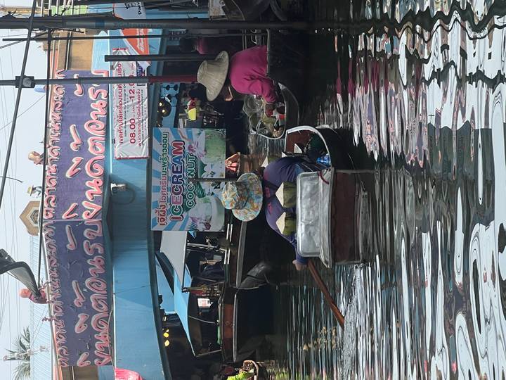 Small wooden boats crowd a canal at Damnoen Saduak Floating Market, one selling coconut ice cream.