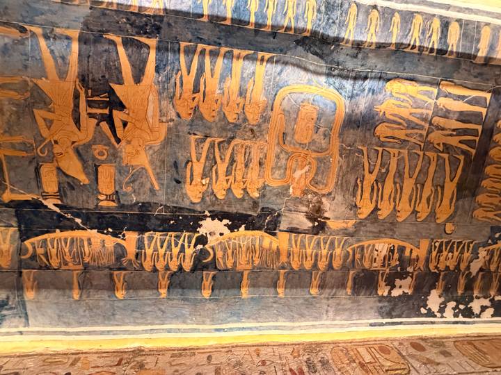 Intricately painted ancient Egyptian ceiling art with detailed blue and gold figures and glyphs.