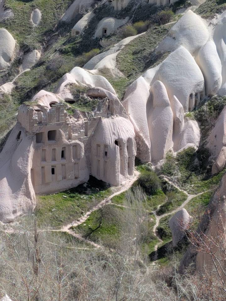 Eroded pink-beige rock formations in Cappadocia reveal ancient cave dwellings carved into the cliffs.