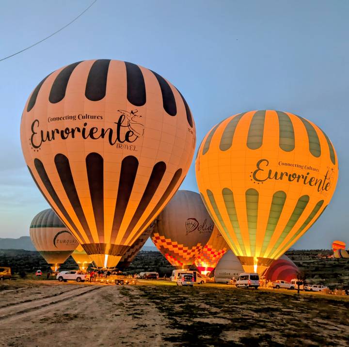 Illuminated hot-air balloons prepare for lift-off in Cappadocia during the early dawn light.