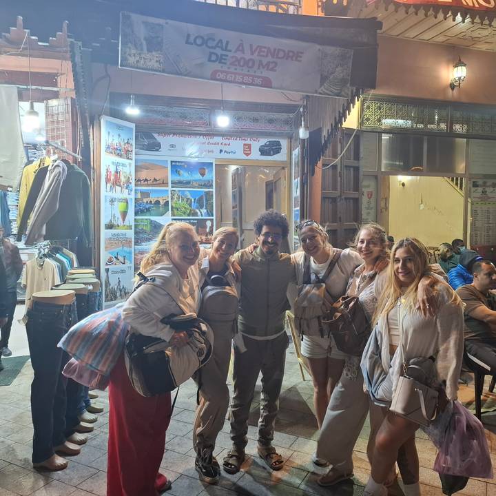 Group of cheerful travelers posing outside a brightly lit souvenir shop at night