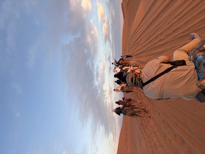 Caravan of tourists riding camels across sand dunes at dusk