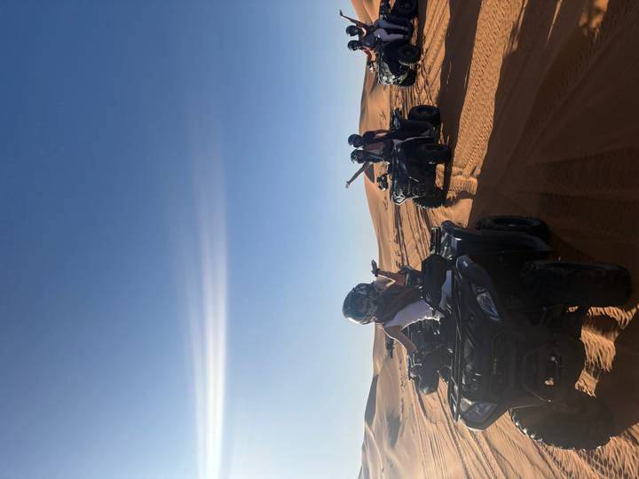 People driving quad bikes over open desert sands under clear sky