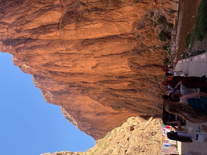 Visitors walk along towering ochre cliffs of a narrow canyon with river below