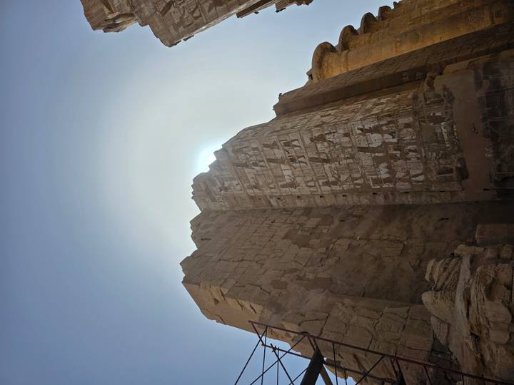 Sunlight halos a towering carved wall of an ancient Egyptian temple viewed from below.