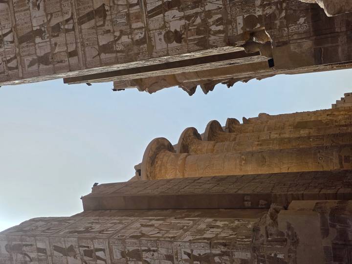 Massive papyrus-shaped columns line a sunlit passageway in an ancient Egyptian complex.