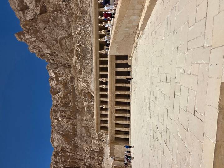 The terraced facade of Hatshepsut’s Temple nestles beneath towering desert cliffs under a deep blue sky.