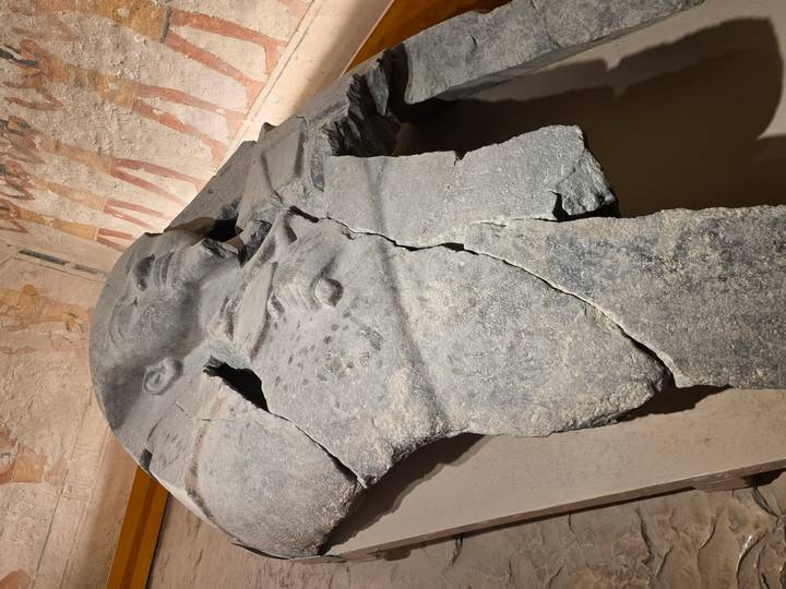 A shattered stone sarcophagus rests in a museum display against walls of ancient art.