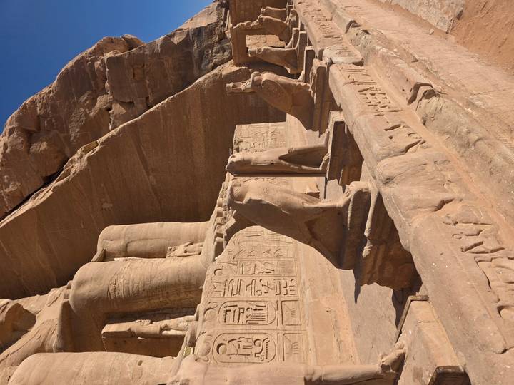 Stone falcon statues stand guard before the colossal legs of Abu Simbel’s seated pharaohs.