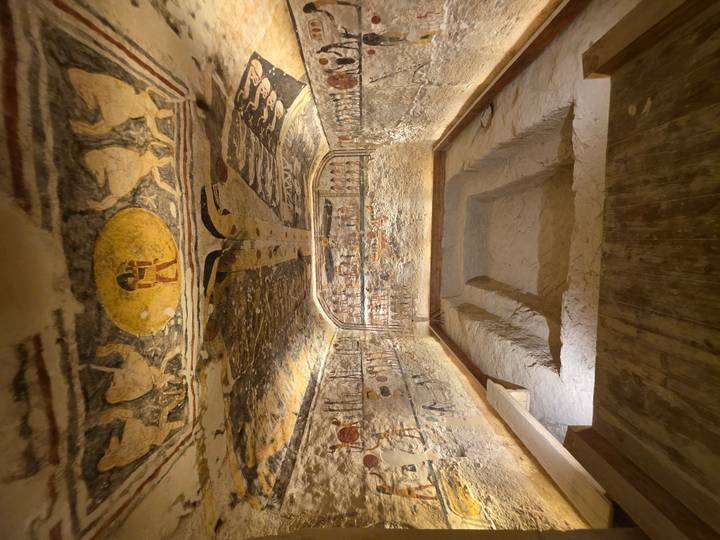 An elaborately painted burial chamber with sunken floor lies illuminated within an Egyptian tomb.