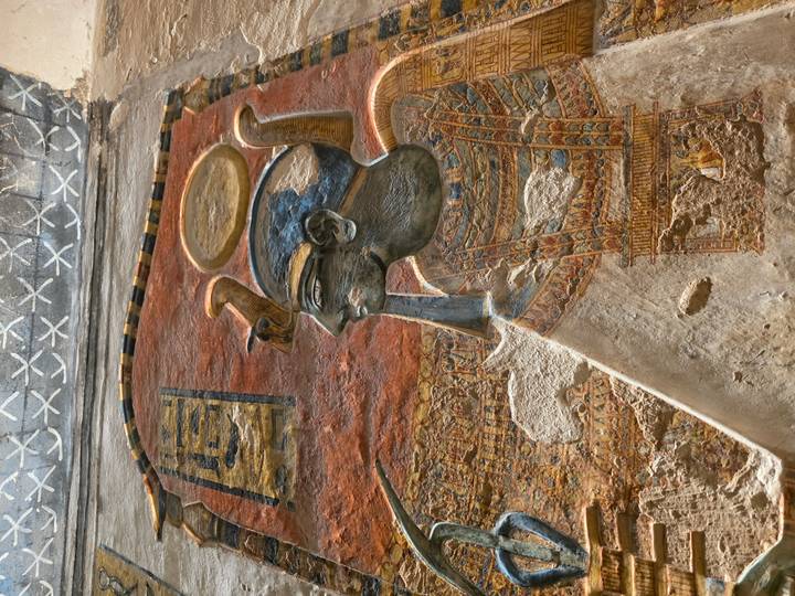 A vividly colored relief of an Egyptian deity with solar disk stands out on a temple wall.