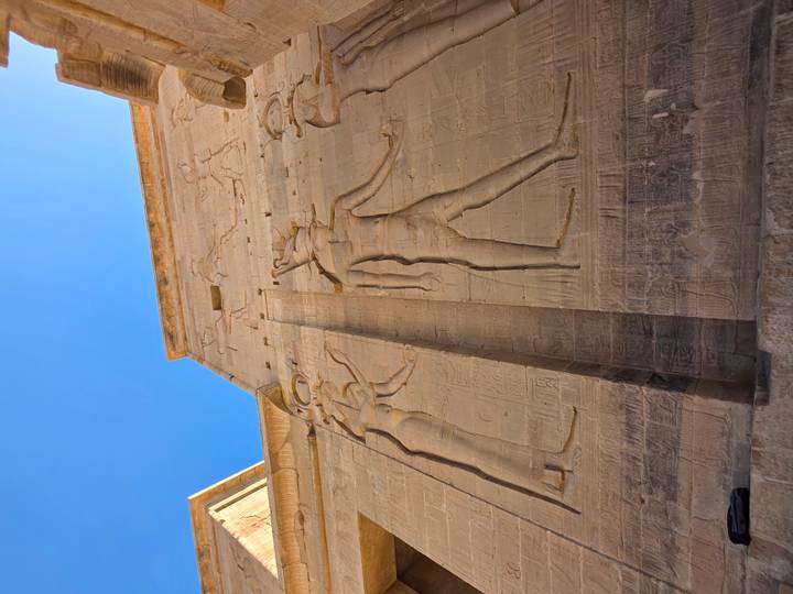 Gigantic bas-reliefs of Egyptian gods adorn the sandstone walls of Philae Temple under a clear sky.