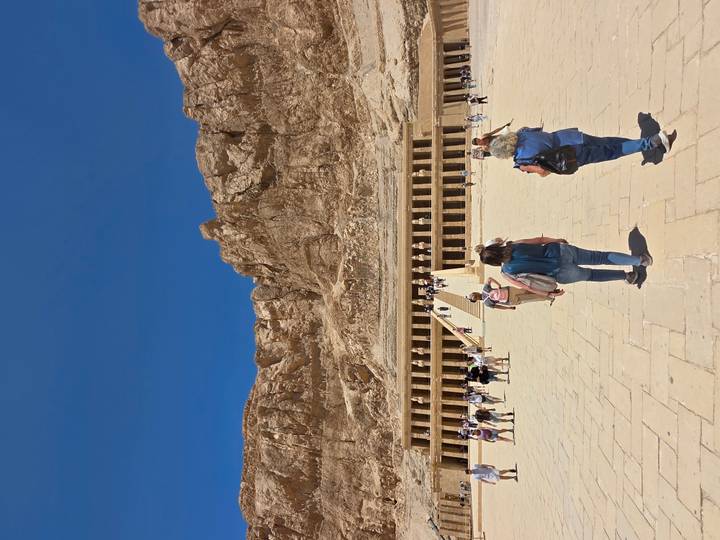 Tourists approach the grand Temple of Hatshepsut against towering desert cliffs.