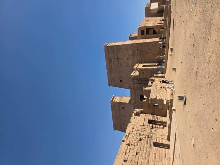 Philae Temple’s pylons and courtyards stand amid a sandy landscape with scattered visitors.