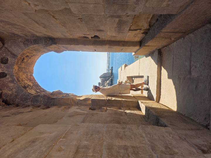 A traveler poses in a stone archway overlooking the shimmering Nile and Philae ruins.