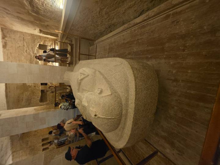 Visitors view a large stone sarcophagus displayed inside an ancient Egyptian tomb chamber.