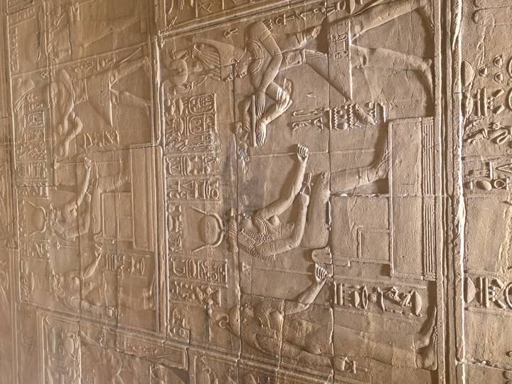 Close-up of detailed wall relief hieroglyphs featuring Egyptian deities in sandstone.