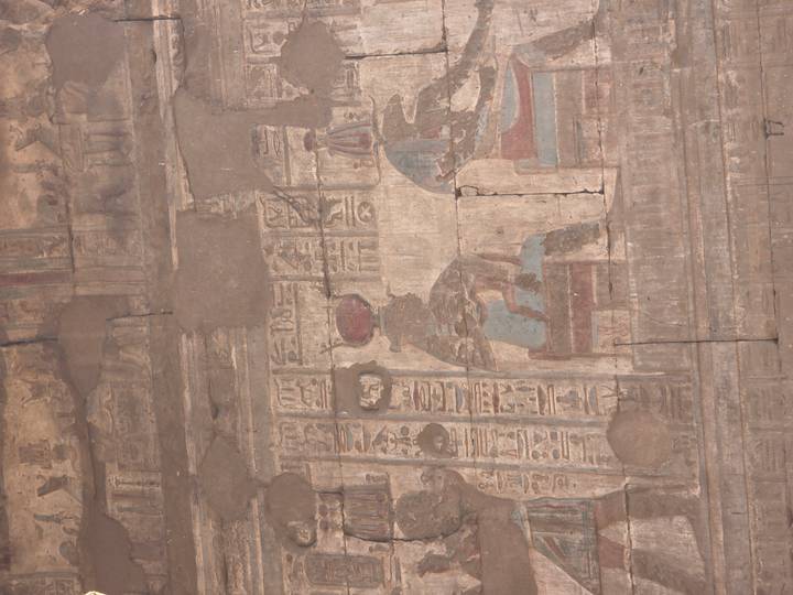 Ancient painted mural with faded colours and hieroglyphs on cracked wall inside Egyptian temple.