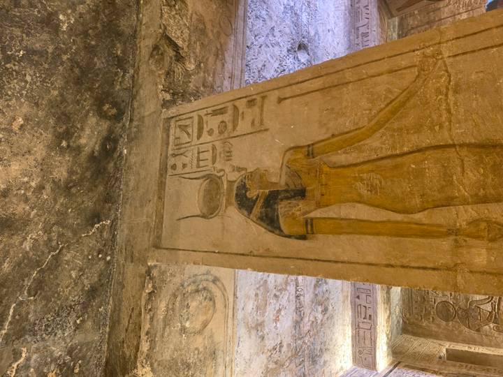 Painted relief of Egyptian goddess on column inside a tomb with yellow lighting.