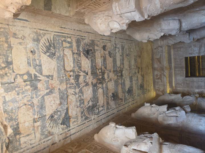 Decorated ceiling with vulture and wing motifs flanked by statues inside the Abu Simbel temple interior.